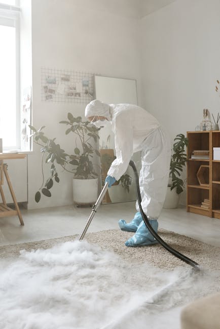 A professional cleaner from Lampton Carpet Cleaners dressed in white protective gear, including a full-body suit, face mask, and blue shoe covers, is performing deep surface cleaning on a beige carpet